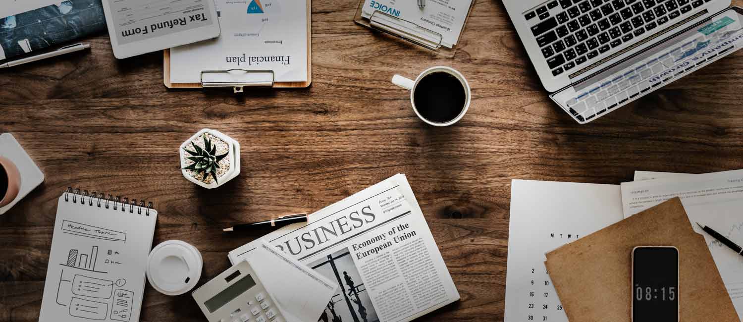 table with coffe, newspaper, pen, calculator, buisness plan on it.